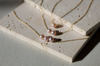 Three gold chain necklaces with blush pink pearls - single, double, and triple pearl styles.