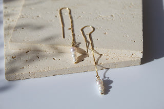 Gold threader earrings with delicate chain and three white cascading pearls on a textured surface