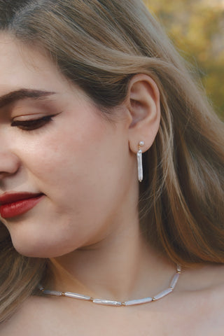 Model wearing an elongated pearl drop earring in gold with a matching necklace.