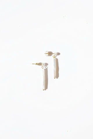 Pair of minimalist gold pearl stud with an elongated pearl drop earring on a white background. 