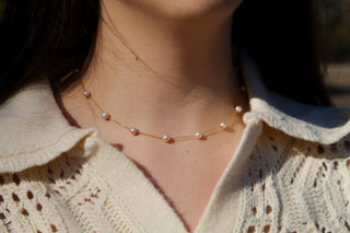Close-up of a gold chain with evenly spaced blush-pink pearls worn at the collarbone. 